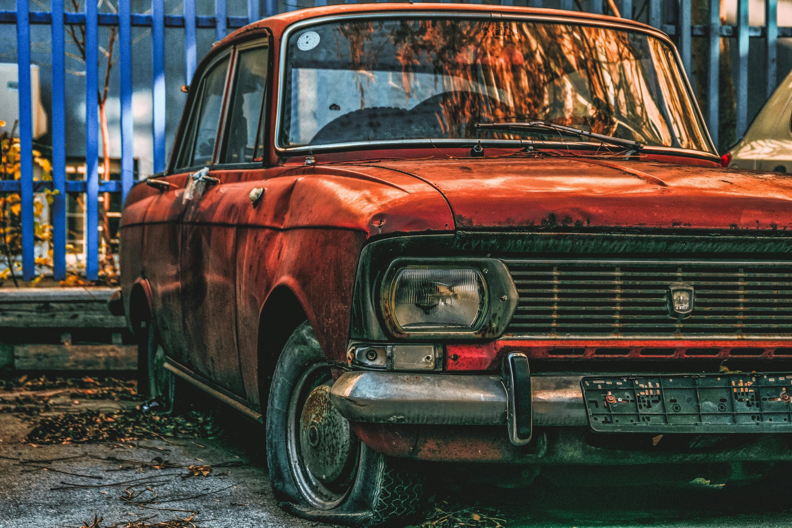 An atmospheric image of a rust-covered vintage car parked in an urban outdoor space.